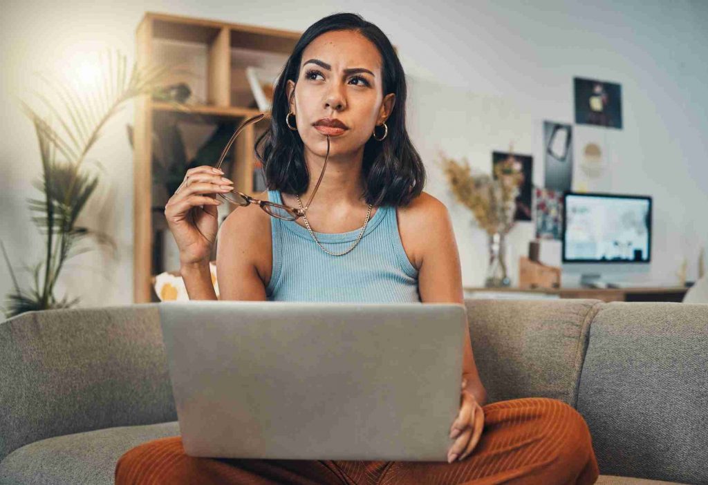 woman thinking while using laptop in living room at home